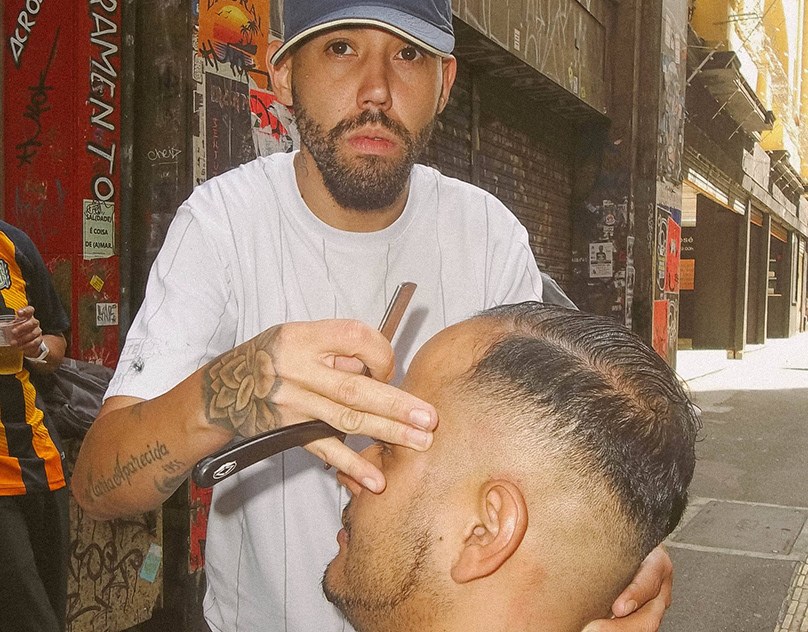 Barbeiro de navalha em punho fazendo a barba de um cliente na rua